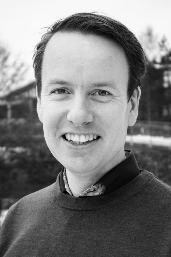 Øyvind Sandåker smiler mot kamera. Svart-hvitt portrett.
